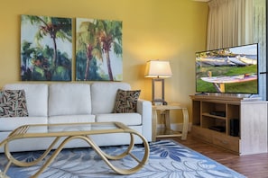Un salon avec un canapé, un téléviseur et deux tableaux accrochés au mur.