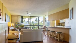 A spacious living room with a sofa, a TV, and a dining area with chairs and stools. - Maui Sunset Vacation Rentals- B318 (Kihei)
