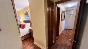 A narrow hallway with wooden flooring leading to a bedroom with a bed and nightstands. - Oceanfront condo on wing of complex near beach, pool - Perfect for Sunsets (Kihei)