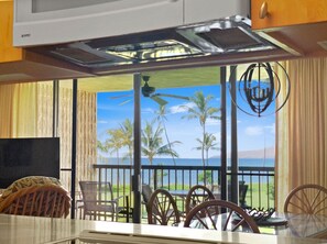 A kitchen with a view of a tropical landscape, including palm trees and a body of water. - Oceanfront condo on wing of complex near beach, pool - Perfect for Sunsets (Kihei)