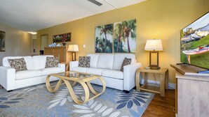 A living room with a white sofa, two side tables with lamps, a coffee table, and a ceiling fan. - Oceanfront condo on wing of complex near beach, pool - Perfect for Sunsets (Kihei)