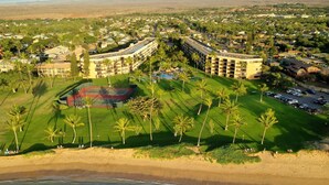 Ein Luftbild eines Resorts mit mehreren Gebäuden, einem Tennisplatz und direktem Zugang zum Strand.