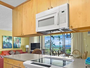 A kitchen with a microwave, a tablet, and a dining area with a view of the beach. - Maui Sunset Vacation Rentals B419 (Kihei)