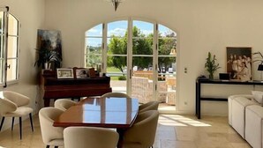 A spacious dining area with a large table and chairs, a chandelier, and a view through a glass door to the outdoors. - La Soleillade Aixoise (Aix-en-Provence)
