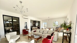 A spacious living room with a large sofa, a coffee table, and a red armchair. There is a dining area with a piano and a plant on a side table. - La Soleillade Aixoise (Aix-en-Provence)