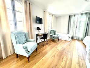 A hotel room with two light blue armchairs, a small table with a lamp, a bed with a white bedspread, and a flat-screen TV mounted on the wall. - La Soleillade Aixoise (Aix-en-Provence)