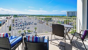 A balcony with wicker furniture, a view of a parking lot, and distant buildings.