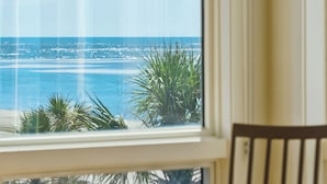 Une vue depuis une fenêtre donnant sur une plage bordée de palmiers et l’océan.