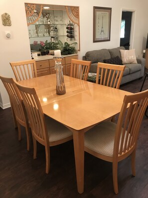 A dining area with a wooden table and chairs, a decorative candle holder, and a kitchen area with wine racks and a mirror.