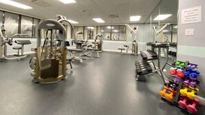 Ett gym med olika typer av träningsutrustning, inklusive en knäböjsställning, hantlar och styrketräningsmaskiner.