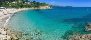 A coastal scene with clear turquoise waters, a sandy beach, and rocky outcrops.