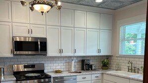 Une cuisine avec des meubles blancs, des appareils en acier inoxydable, un tapis à motifs et un plafond décoratif.