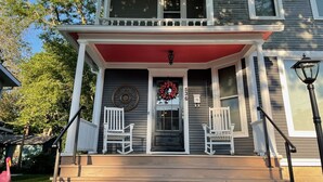 Une maison à deux étages avec un porche, deux fauteuils à bascule, une couronne décorative et une boîte aux lettres.
