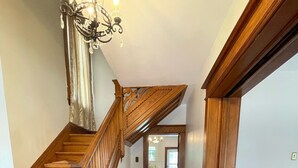 Un escalier en bois orné d’un lustre, un banc en bois et un fauteuil violet dans une pièce dont le sol est recouvert de planches de bois.