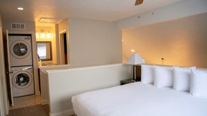 A hotel room with a bed, a nightstand, a lamp, a ceiling fan, and a washing machine.