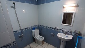 A bathroom with blue and white tiles, a white toilet, a sink, a shower, and a red bucket on the floor.