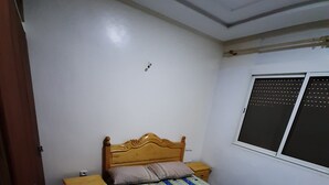 A bedroom with a wooden bed, a nightstand, a window with blinds, and a patterned rug.