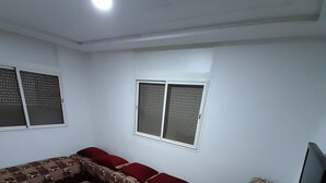 A living room with a sectional sofa, a red and beige patterned rug, a television, and a window with blinds.