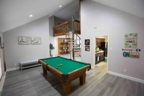 A spacious room with a pool table, a staircase, and a loft area.