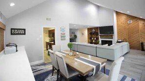 Eine moderne Küche mit Einbauofen, ein Essbereich mit Tisch und Stühlen sowie ein Wohnbereich mit Sofa und Fernseher.