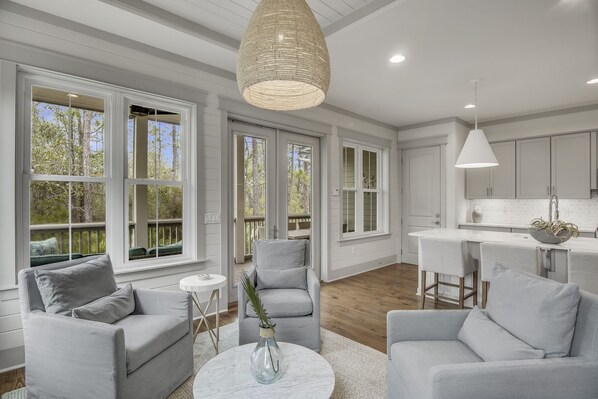 A spacious living room with a grey sofa set, a coffee table, and a large window with a view of trees.
