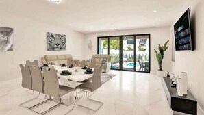 A modern dining area with a white table set for four, a sofa, and a TV mounted on the wall.