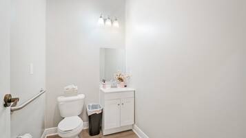 Un bagno con un water bianco, un lavandino bianco e uno specchio sopra, e un cestino.