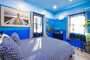 A bedroom with a large bed, a painting of a lighthouse, and a wall mural of sea creatures.