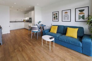 Un salon moderne avec un canapé bleu, une petite table blanche et un coin repas comprenant une chaise et une table.