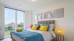 Ein Schlafzimmer mit einem großen Bett, Blick auf die Stadt und gerahmten Bildern an der Wand.