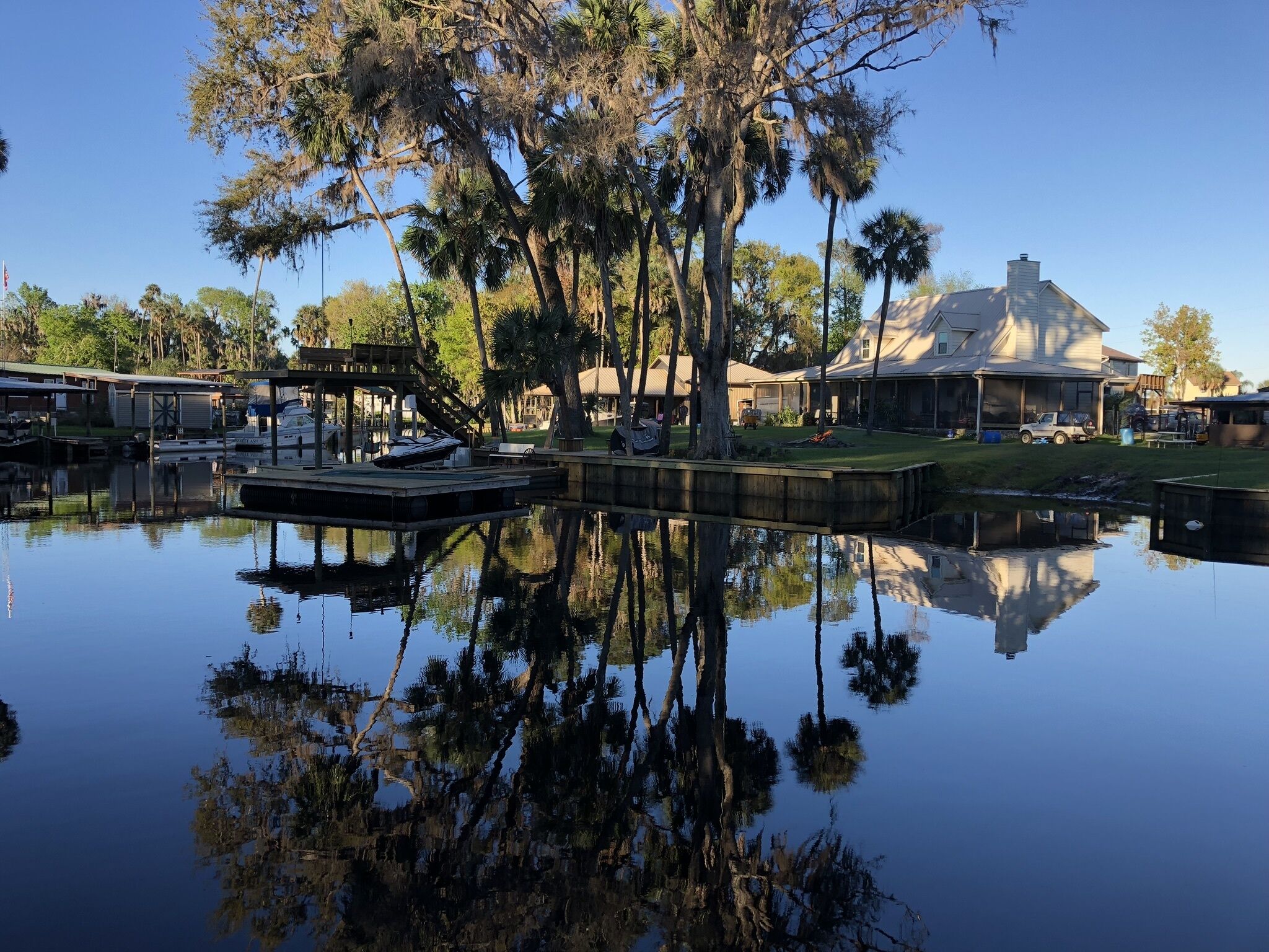 A calm water body reflecting trees and a house with a large roof.