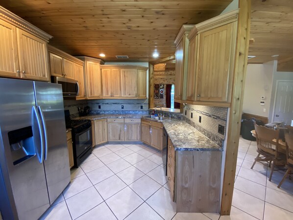A kitchen with wooden cabinets, a stainless steel refrigerator, and a granite countertop. - Springfed Canal on Lake George/ Large 4 Bedroom house on water/Boat Ramp/Hot Tub (SaltSprings)
