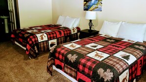 A hotel room with two beds, each with a red and black checkered bedspread featuring animal prints, white pillows, and a painting of a forest stream on the wall. - Lynnhurst Resort Motel #9...Dog Friendly Jet Ski Rentals on site (Murray)