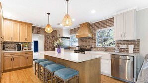 Une cuisine moderne avec des meubles en bois, un îlot central doté de tabourets de bar, des luminaires suspendus et un mur de fond en briques.