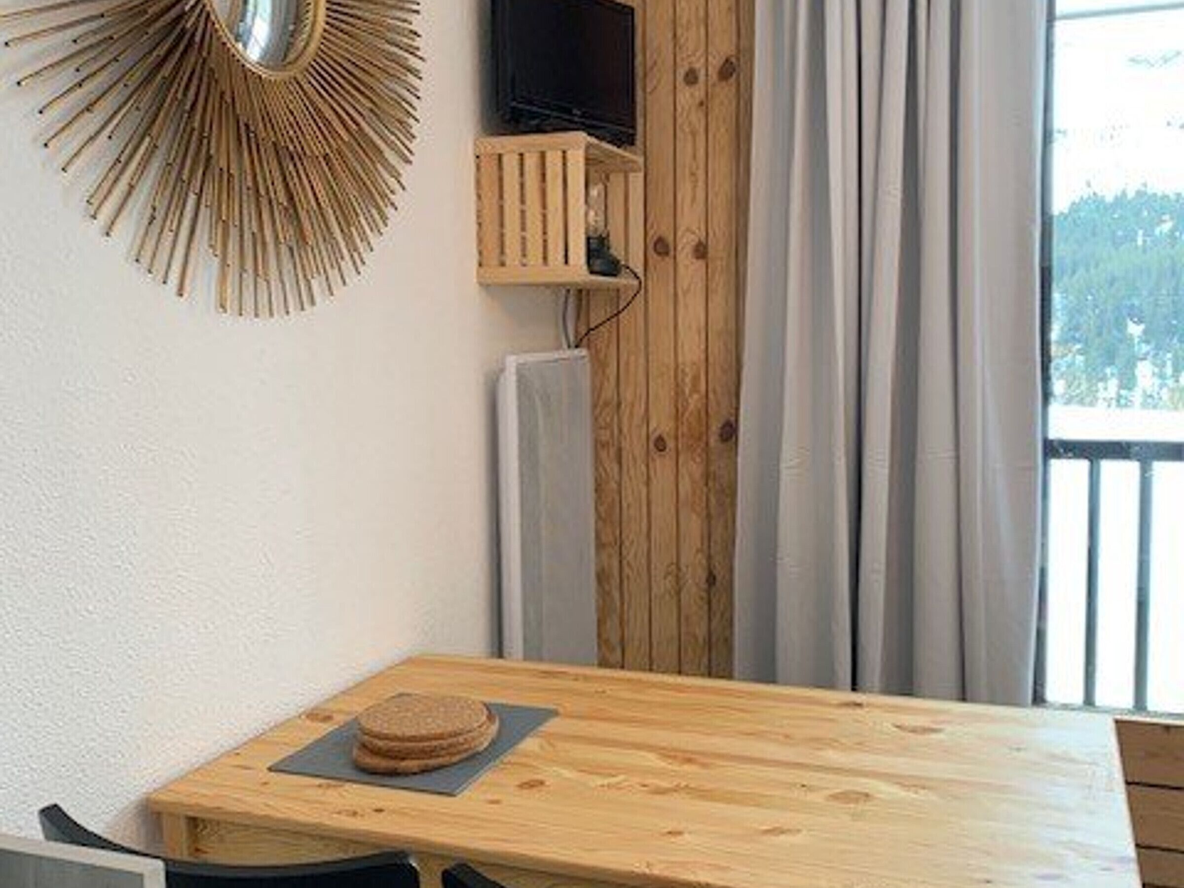 Una mesa de madera con un plato de galletas, un estante de madera con un televisor y una ventana con cortinas.