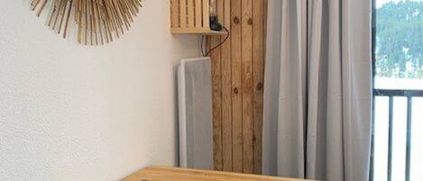 Una mesa de madera con un plato de galletas, un estante de madera con un televisor y una ventana con cortinas.