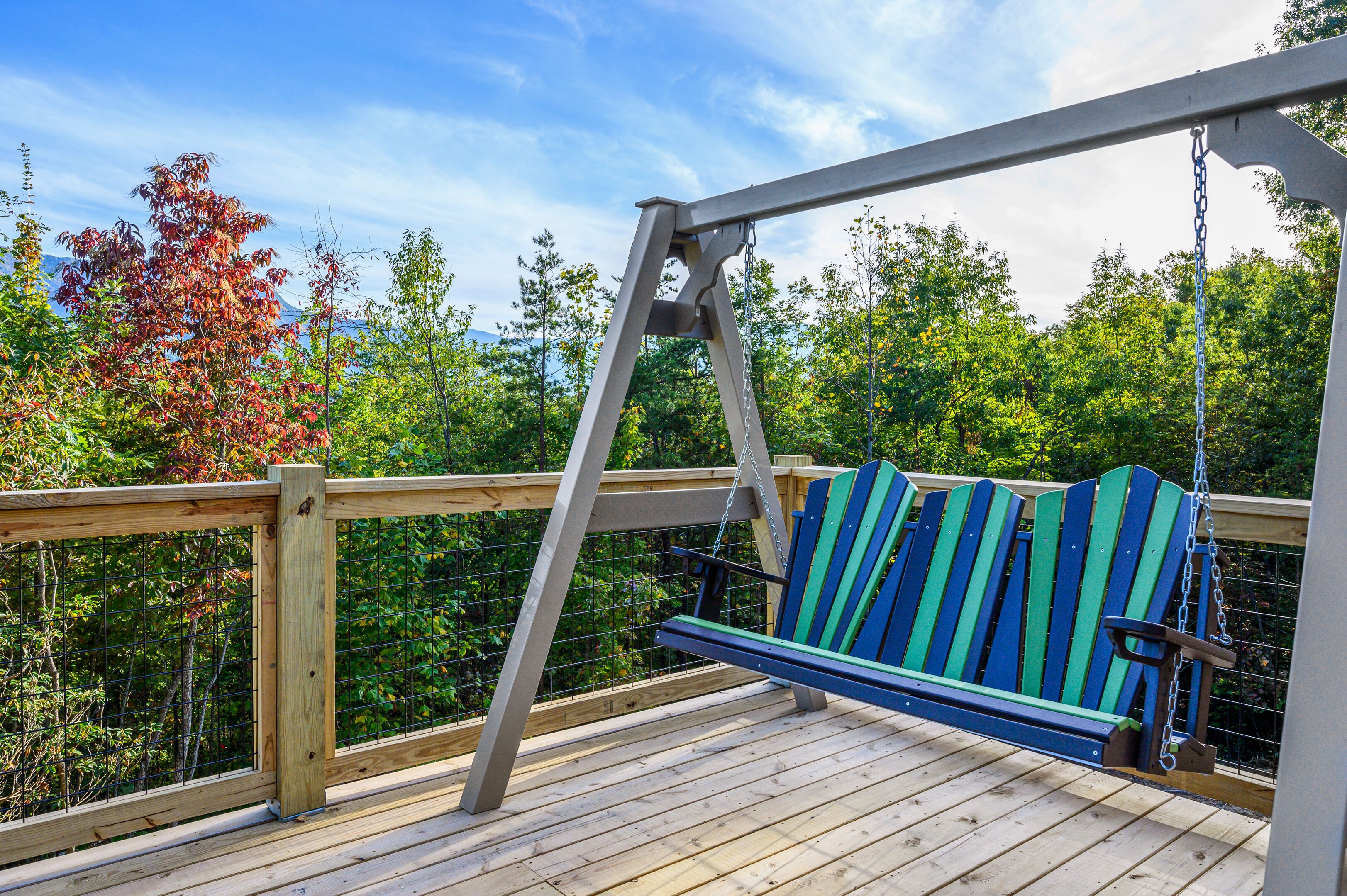 Una terraza de madera con una silla colgante y una barandilla de metal.