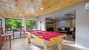A pool table in a room with wooden ceiling and large windows.