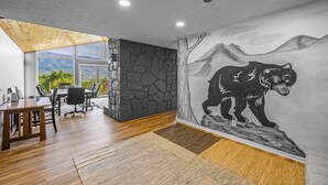A modern office space with a large mural of a bear, a wooden ceiling, and a view of greenery through large windows.