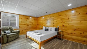A bedroom with a wooden paneled wall, a bed with a white bedspread, a green sofa, and a window with blinds.