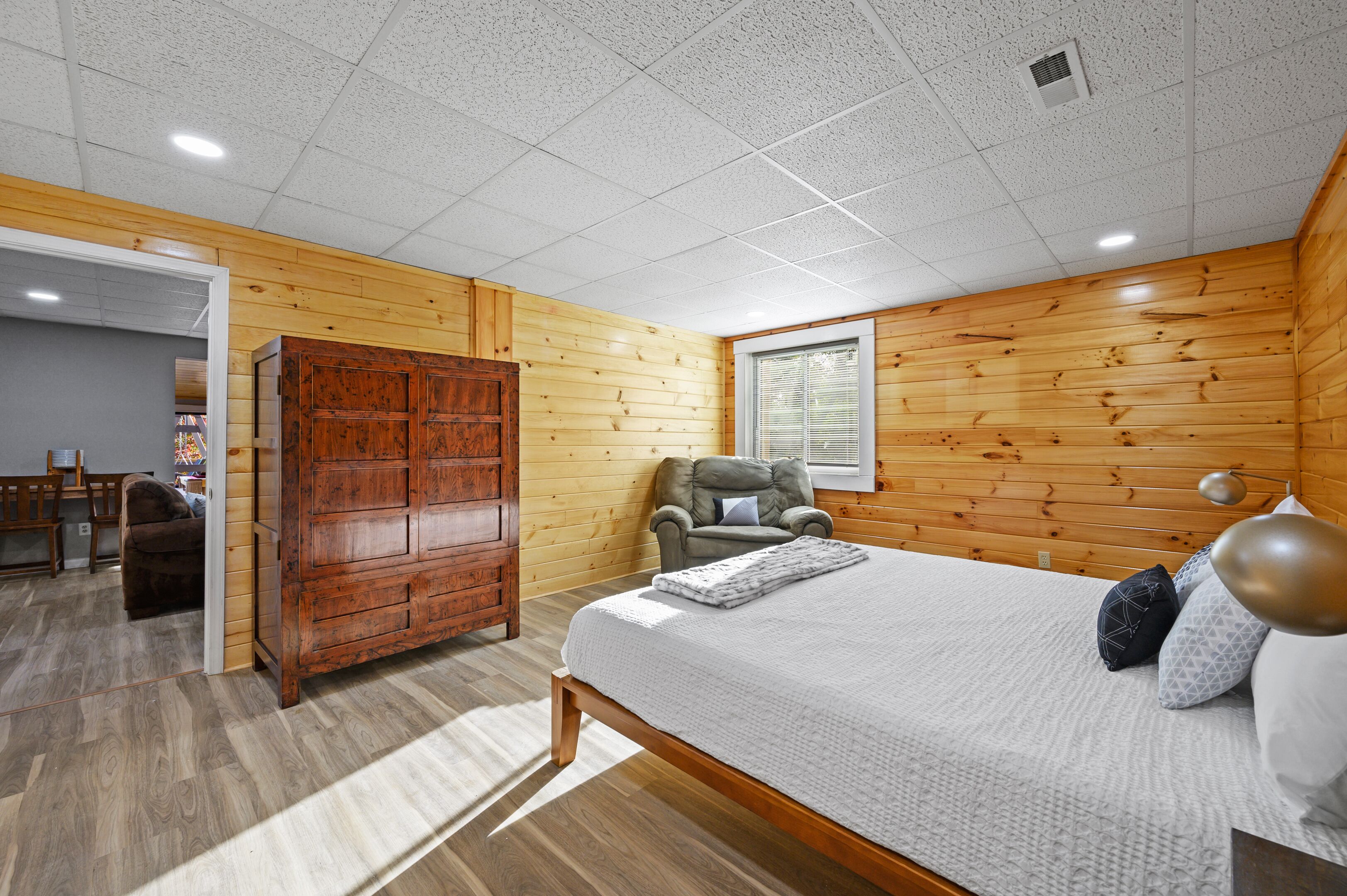 Ein Schlafzimmer mit Holzwand, einem Bett mit Kissen, einem Sessel und einem Kleiderschrank.
