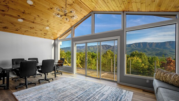 A spacious room with a large sliding glass door leading to a deck, a wooden ceiling, and a view of mountains.
