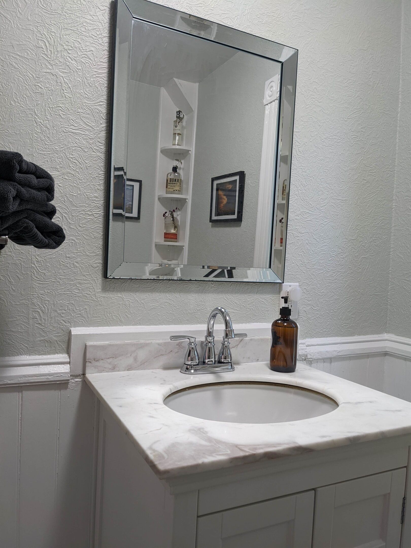 A bathroom with a white marble sink, a mirror, and a shelf with toiletries.