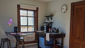 A compact kitchen with a window, a clock, and a wooden door. - Flamingo Suite (Downtown Wolfville) (Wolfville)