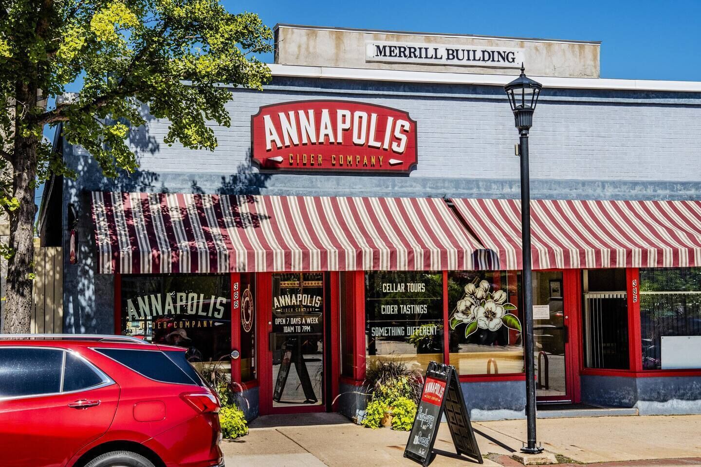 Un escaparate con un toldo a rayas rojas y blancas, un letrero que dice 'ANNAPOLIS CIDER COMPANY' y anuncios que indican 'VISITAS A LA BODEGA' y 'CATA DE CIDRA'.