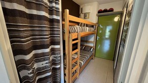 Un couloir étroit avec des lits superposés, une porte verte et un rideau à rayures.