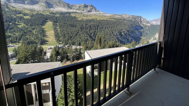 Un balcon offrant une vue sur un paysage montagneux, avec des zones boisées et un ciel dégagé.
