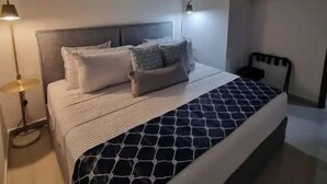 Un dormitorio moderno con una cama, lámparas de noche, un espejo redondo y un estante con toallas.