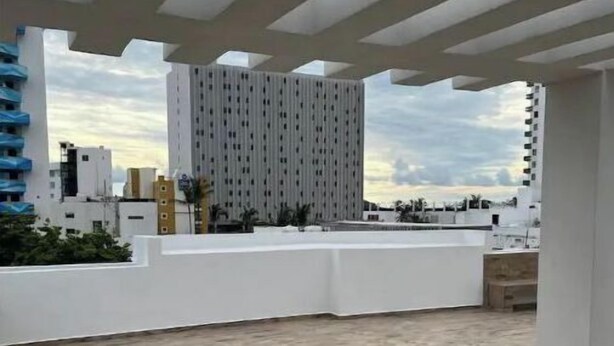 Una terraza en la azotea con piso de madera, paredes blancas y vistas de edificios cercanos.