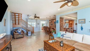 A spacious living area with a staircase, wooden furniture, and ceiling fans. - Sea Watch: 4B/4B Direct Oceanfront Home with Pool Near Downtown Cocoa Beach (Cocoa Beach)